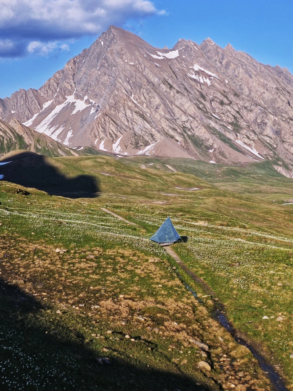 Tente posée sur un alpage du TMB début juin, minuscule sous le sommet et la neige encore présente : une ambiance qui n'existe plus une fois la haute saison lancée